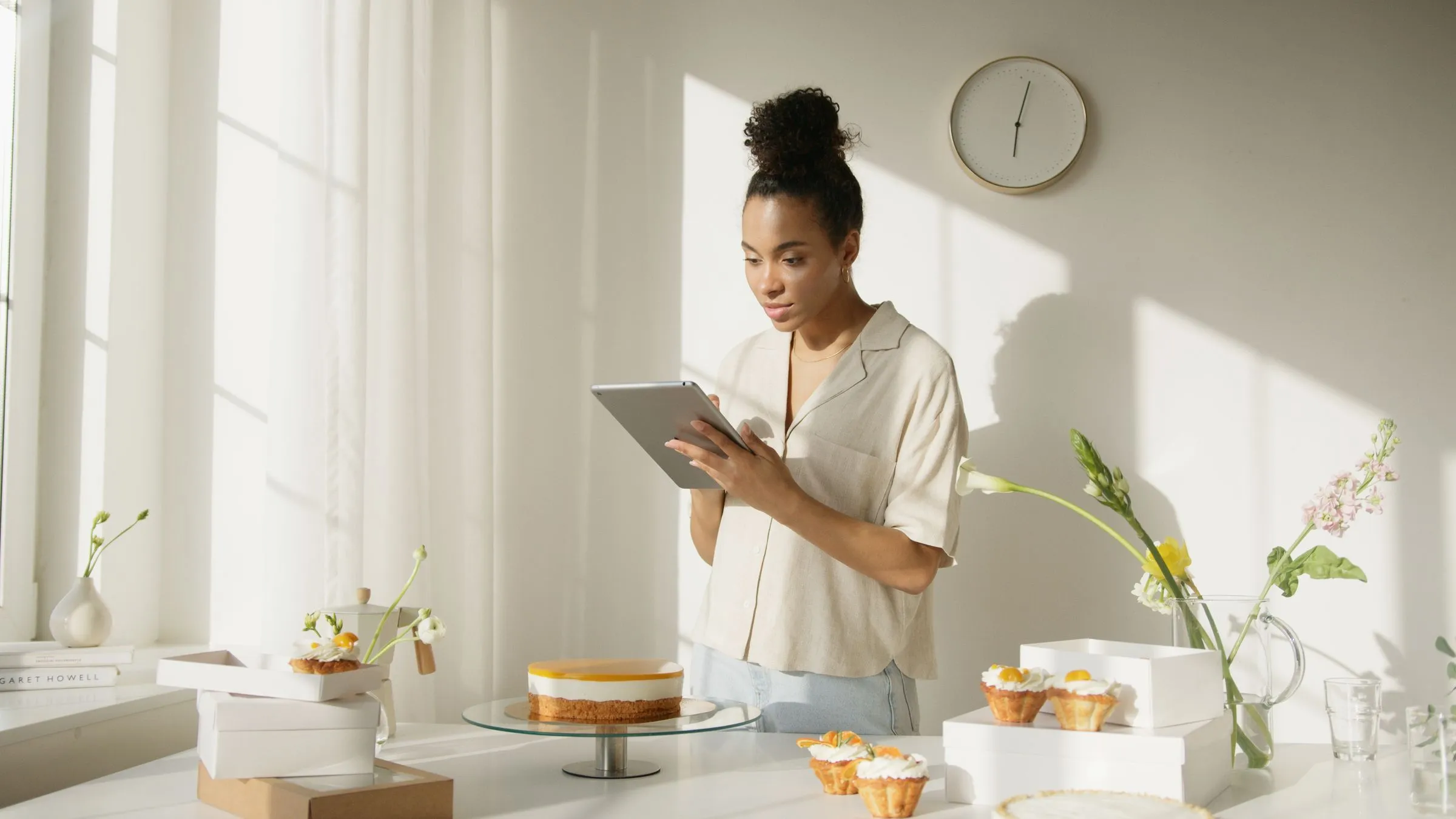 A bakery owner checking figures on a tablet beside a cake on the counter of a bright shop.